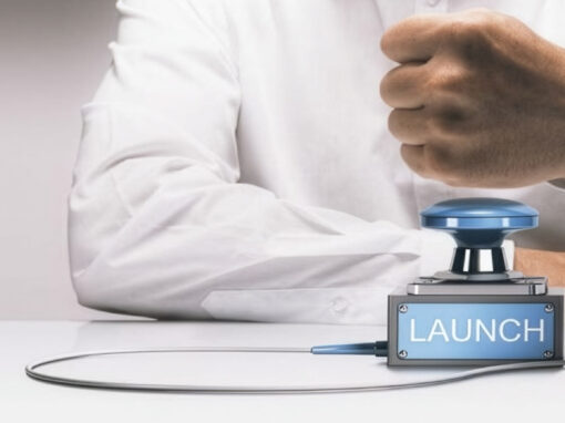 Person pressing a blue launch button next to a small blue rocket on a white table.